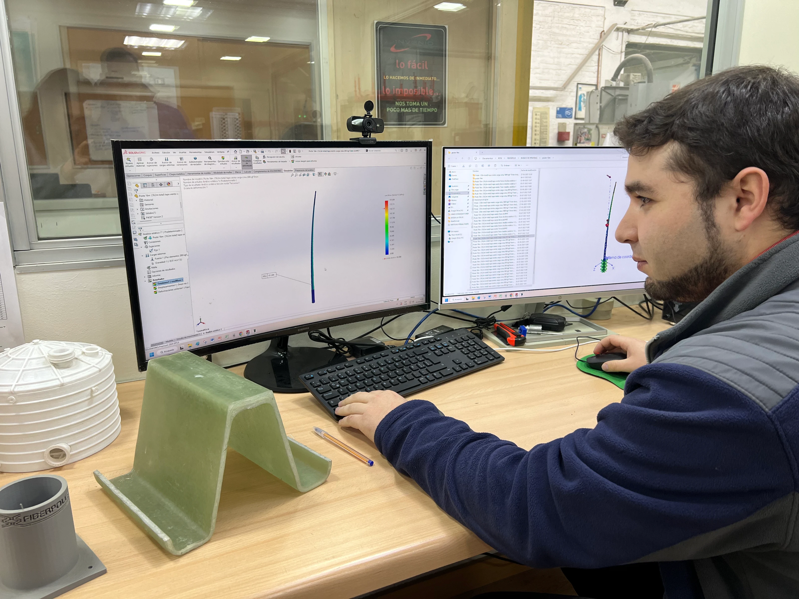 Ingeniero en una estación de trabajo con un modelo de simulación estructural en pantalla y una probeta de laminado FRP sobre el escritorio.