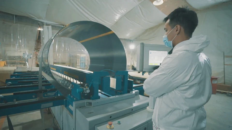 Operario junto a una máquina de filament winding mientras enrolla fibra sobre un mandril cilíndrico.