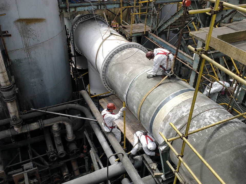 Trabajadores realizando labores sobre un ducto industrial en terreno.