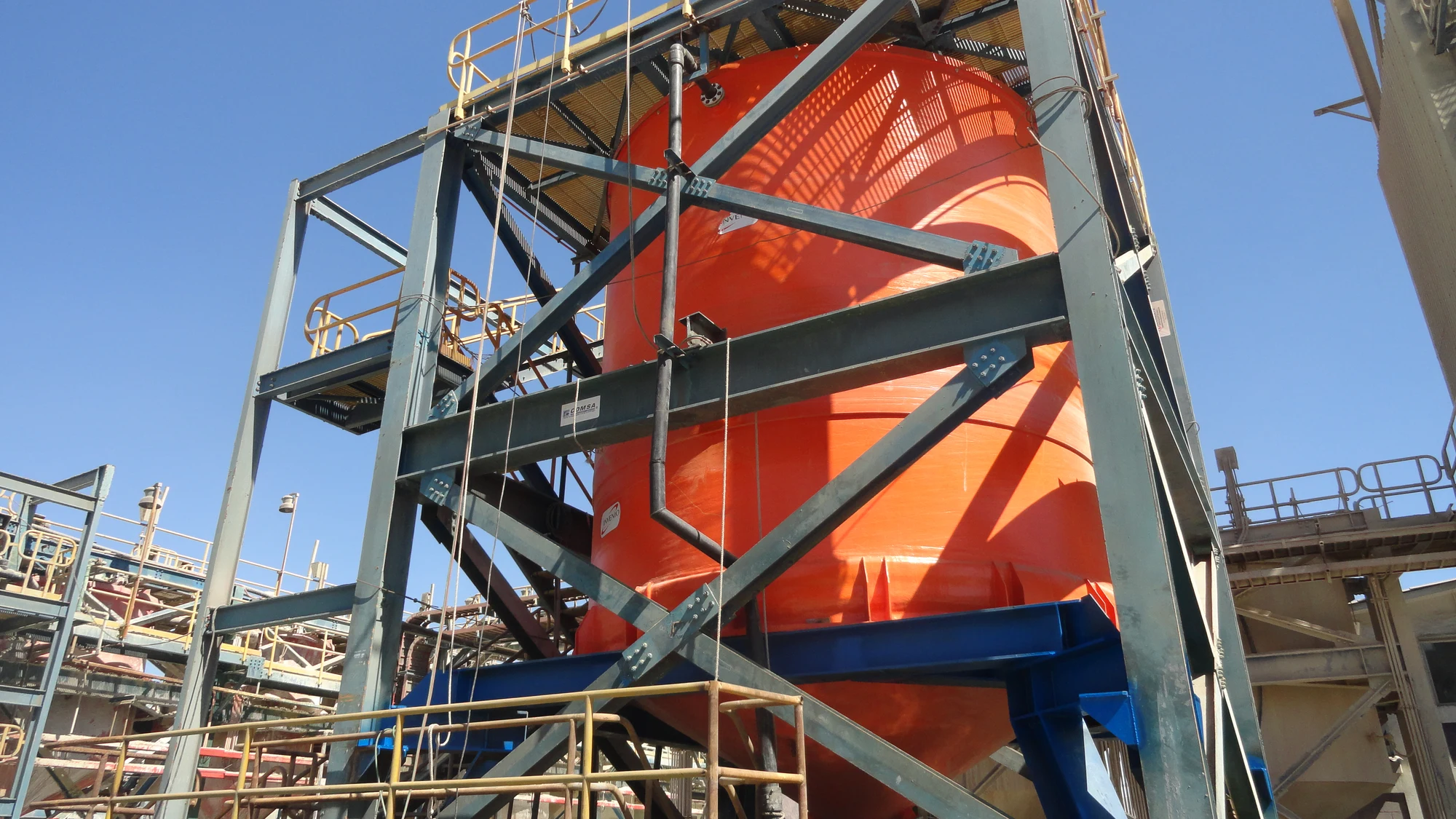 Grúa izando un componente cilíndrico de FRP junto a la estructura de andamiaje de la torre desulfurizadora, en un recinto industrial.
